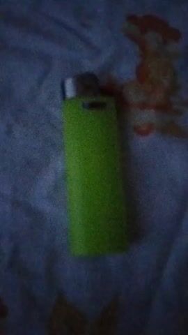 A green lighter is lying on a white surface with orange stains. A hand briefly enters the frame from the bottom left.