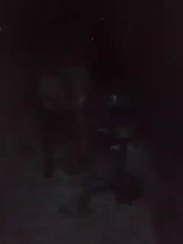 In a very dimly lit environment, a person stands beside what appears to be a bucket. The person seems to be holding and using a stick or rod, possibly stirring something inside the bucket. Due to the extreme darkness, details are difficult to ascertain, but it appears the scene is outdoors, possibly at night. There are other objects nearby, but they are too indistinct to identify with certainty. The person is the main subject of the video and appears to be engaged in a task involving the bucket and the stick.