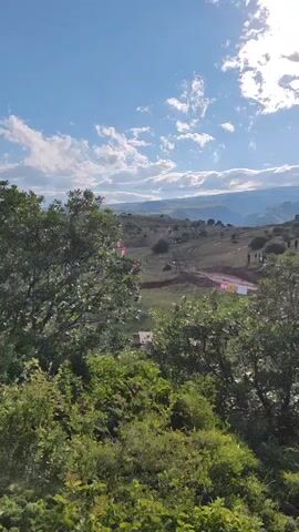 This video captures an off-road racing event taking place in a hilly, grassy landscape under a partly cloudy sky. The time appears to be late afternoon or early evening, given the warm sunlight casting long shadows. The scene is set in Antarut, Armenia, as indicated by the visual cues of the rugged terrain and what seems to be a rural or mountainous area.

The primary subjects are the off-road vehicles, likely ATVs or similar recreational vehicles, navigating a marked course. Several vehicles are visible in motion, kicking up dust on the dirt tracks. Numerous people are present, spectating or participating in the event. They are scattered across the hillsides, some clustered near the course and others further afield. Red flags, possibly marking turns or boundaries, are strategically placed along the track.

The event appears to be a competitive race or a recreational off-road gathering. The setting is a natural, untamed environment, with sparse vegetation and a vast open sky. The weather is fair, with the sun occasionally breaking through the clouds, creating a dynamic play of light and shadow. The mood seems to be one of excitement and activity, typical of a sporting event.

While there is no clearly legible text visible on the vehicles or banners, the presence of flags and marked courses strongly suggests an organized event. The overall impression is a vibrant outdoor activity set against a scenic, natural backdrop.
