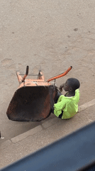 Youth sits in overturned wheelbarrow on Bukuru street