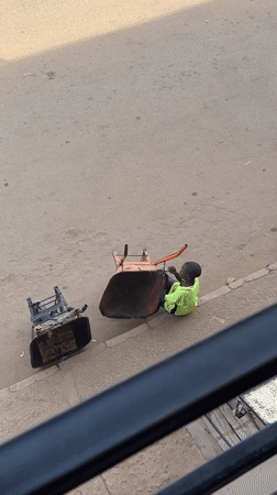 Youth sits in overturned wheelbarrow on Bukuru street