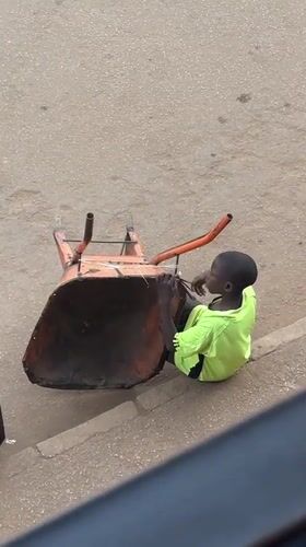 Youth sits in overturned wheelbarrow on Bukuru street