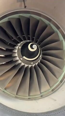 This media file showcases an airplane parked on an airport tarmac under a clear, bright blue sky, suggesting a sunny day. The camera focuses on the aircraft's powerful jet engine, with its intricate fan blades visible from the front. The perspective then pans to reveal the plane's landing gear, including its robust wheels and suspension system.

The surrounding environment includes concrete tarmac, yellow and white striped ground markings, and orange traffic cones, typical of an airport operational area. In the background, a mobile stairs unit is positioned near the aircraft's wing, and further beyond, desert-like terrain with sand dunes can be seen under the intense sunlight. The overall impression is one of an aircraft at rest, likely undergoing pre-flight checks or waiting for passengers, in a warm, arid location like Cerro Colorado, Peru. No people are visible in the media.

There is some visible text on the aircraft's body and the stairs. On the stairs, the word "TELMA" is visible. On the aircraft's fuselage near the landing gear, there appears to be a yellow warning label with black text, although the text itself is not legible. Another label on the wing has illegible white text on a black background.