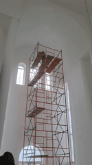 Painter works on scaffolding in white arched building