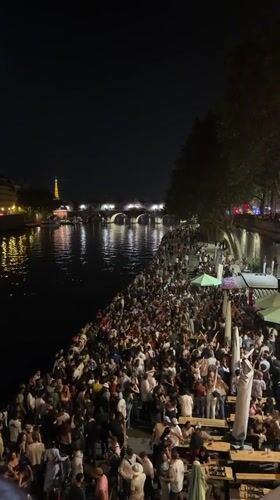 Crowds gather along Seine riverbank in Paris evening