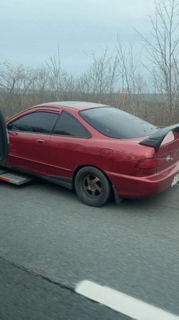 Burgundy Integra towed by U-Haul truck on highway