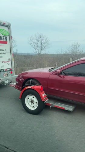 Burgundy Integra towed by U-Haul truck on highway