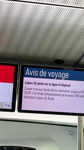 The video shows a close-up of a digital display screen mounted on the ceiling of a public transportation vehicle, likely a train or bus. The screen displays a travel advisory in French. The advisory states that the Lajoux JU stop on line 41 has been displaced due to construction. The restriction is in effect until June 19, 2026, at 23:59. The replacement stop is located 100 meters in the direction of Lajoux JU school. The background of the video shows the interior of the vehicle, including the textured ceiling and a metal support pole. The lighting suggests an indoor environment.