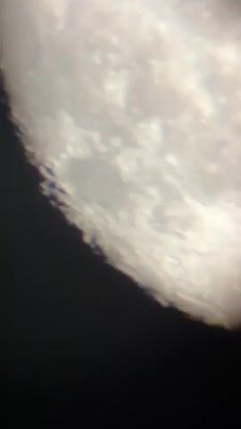 The video displays a close-up, somewhat blurred, view of the Moon's surface. The dominant subject is the Moon, with its craters and varied terrain clearly visible along the edge that meets the darkness of space. There are no people or specific objects other than the celestial body itself. The scene is set in outer space, implied by the presence of the Moon against a black background.

The activity taking place is observational, as if looking through a telescope. There is no discernible time of day or weather, as it is a view of space. The location context of Târgu Neamț, Romania, is relevant to the observer's perspective but not directly depicted in the visual content. No emotions are conveyed by the imagery. There is no visible text in the media file.