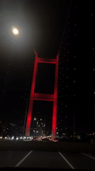 Car crosses red-lit Bosphorus Bridge in Istanbul at night