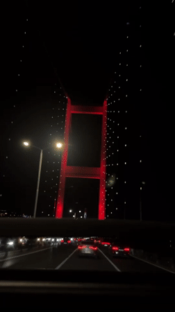 Car crosses red-lit Bosphorus Bridge in Istanbul at night