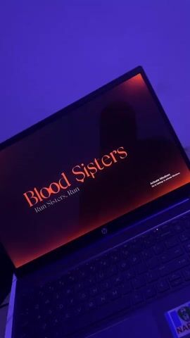 A laptop is open in front of a purple background. The laptop screen displays the words "Blood Sisters. Run Sisters. Run" in orange text. A silhouette of a person's head and shoulders is visible on the screen, superimposed over the text. The laptop has a black keyboard and a dark gray casing. To the right of the screen, a watermark reads "Activate Windows." The video then transitions to a view of a bridge spanning over water.