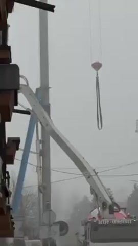 The video shows a foggy day scene with construction equipment.  A crane is visible in the fog, with its arm extended horizontally. A boom lift, partially visible, is positioned near a building under construction. The overall atmosphere suggests active construction work in limited visibility conditions.