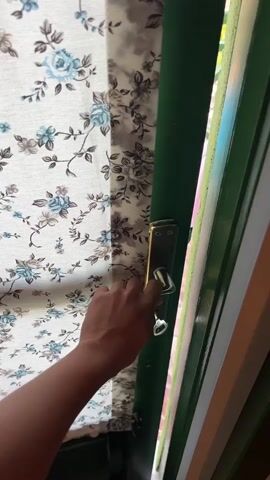 The video shows a hand opening a door. Beyond the door is a balcony with a swimming pool and trees. In the background, a body of water and hills are visible. The sky is clear and blue, suggesting it is daytime.