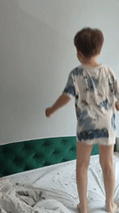 Morning playtime: boy jumps on bed, cat rests nearby