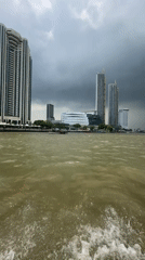 Morning boat ride captures Bangkok riverside skyline under cloudy skies