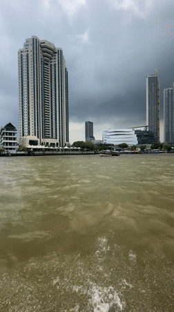 Morning boat ride captures Bangkok riverside skyline under cloudy skies