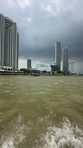 Morning boat ride captures Bangkok riverside skyline under cloudy skies
