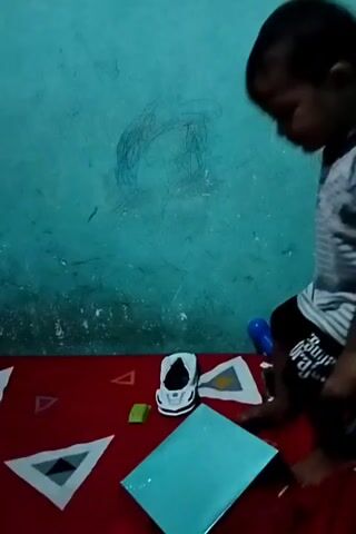 A young boy with dark hair and a striped t-shirt kneels on a red rug in front of a turquoise wall. He is playing with a toy car and a shiny, flat object. The wall has crayon marks on it.