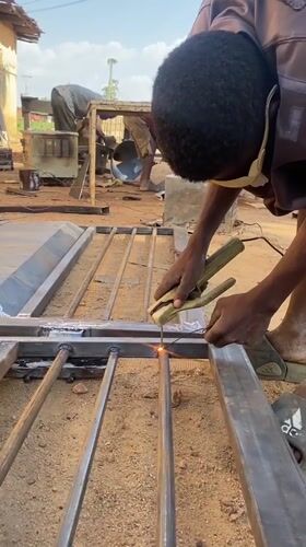 Metal workers weld gates in outdoor workshop, Nigeria