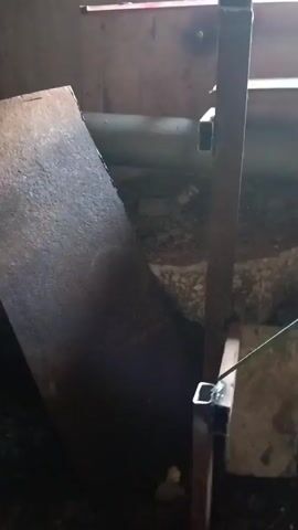 A welding torch is actively in use, emitting bright sparks and a plume of smoke. The welding is occurring on a metal structure, possibly for construction or repair. The background appears to be an industrial or workshop setting, with various metal and debris visible. The lighting is dim, with the bright light from the welding process illuminating the immediate surroundings. The video captures the intense heat and activity of welding.