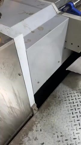 The video shows a close-up, eye-level shot of an industrial machine in operation. The machine is primarily constructed of metal, with some components painted white and others appearing to be stainless steel. The scene is brightly lit, suggesting an indoor factory or workshop setting.

The central focus is a section of the machine where a large, flat piece of cardboard is being fed through. There are rollers, some with orange and blue elements, moving the cardboard along. Above the cardboard, there is a complex arrangement of metal parts, including shafts, gears, and what appear to be cutting or scoring blades. A bright red, coiled tube is also visible at the top left of the frame, likely a pneumatic or hydraulic hose.

There is no visible text within the frame. The overall impression is one of a functional, automated industrial process, likely involved in the manufacturing or packaging of cardboard products. The camera is static, providing a steady view of the machine's activity. The metal surfaces of the machine show some signs of wear and dirt, indicating it is a working piece of equipment. The lighting is even and shadowless, with no indication of natural light or time of day. The location context of Oral, Kazakhstan, does not provide any visual cues within the video itself. The emotions conveyed are neutral, focusing on the mechanical operation.