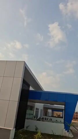 The video shows a modern building with white and blue exterior elements against a sky with scattered clouds. A construction crane is visible in the background. The camera angle is looking up towards the sky and the building. There are no people or discernible actions taking place. The environment appears to be an outdoor setting, possibly a construction site or an area with new development.