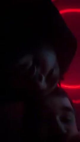 The video shows a man singing into a microphone, with red or purple neon lighting behind him. The first shot has his face obscured by the microphone. The second shows the lighting, and the man's face, bathed in blue light. The third shows the man singing into the microphone, bathed in red light. The final shot shows his face closer up, still bathed in red and purple light.