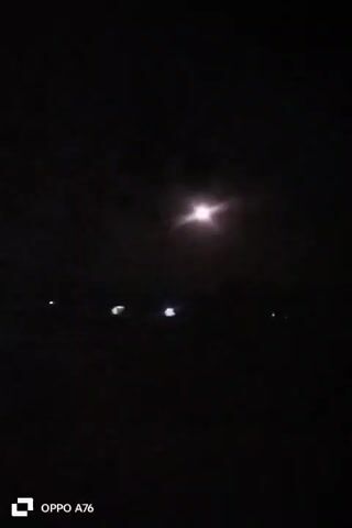 A blurry nighttime video shows a bright light in the dark sky, possibly the moon or a streetlight. Below the light, indistinct shapes suggest distant objects or lights. The bottom left corner of the frame displays a logo indicating the recording device is an OPPO A76.