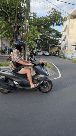 Helmeted scooter rider travels Kuta road in casual attire