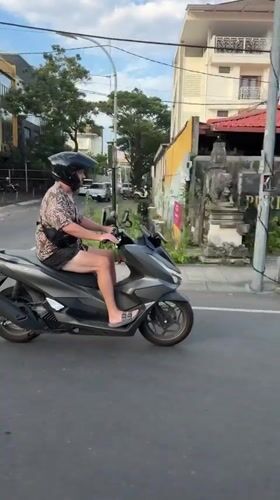 Helmeted scooter rider travels Kuta road in casual attire
