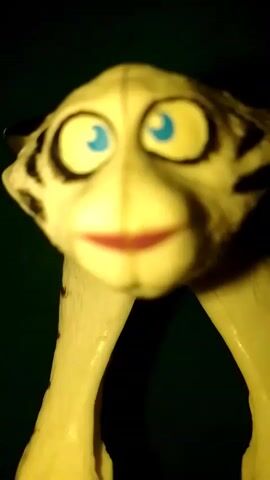 THE VIDEO SHOWS A CLOSE-UP, SLIGHTLY BLURRED SHOT OF A WHITE, PLASTIC TOY OR FIGURINE. THE TOY HAS LARGE, ROUND, BLUE EYES WITH THICK BLACK EYELIDS. IT ALSO HAS A SMALL, REDDISH-PINK MOUTH. THERE ARE DARK MARKINGS ON THE SIDES OF ITS HEAD, RESEMBLING TIGER STRIPES. THE TOY APPEARS TO BE STANDING ON TWO THIN, WHITE LEGS. THE BACKGROUND IS DARK AND BLURRY, SUGGESTING A LOW-LIGHT ENVIRONMENT. THE CAMERA SEEMS TO BE MOVING SLIGHTLY, CAUSING A GENTLE SHAKE IN THE IMAGE.