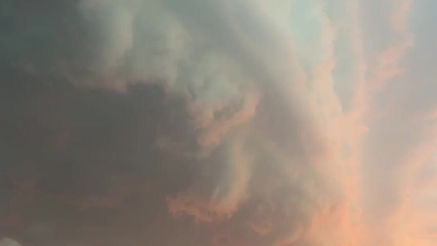 The video is a close-up of a stormy sky with dark, turbulent clouds. The clouds appear to be illuminated by the setting sun, casting a pinkish hue on some parts of the sky. The clouds are dense and thick, suggesting an impending storm. The camera is focused on the movement and texture of the clouds, creating a sense of awe and perhaps apprehension. There are no people, objects, or specific actions visible in the video, only the dramatic spectacle of the natural environment.
