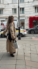 Woman in trench coat walks Moscow sidewalk Friday afternoon