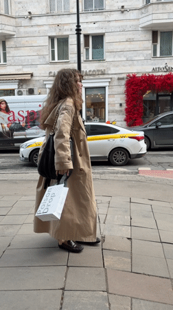Woman in trench coat walks Moscow sidewalk Friday afternoon