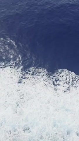 This is a short video clip of the ocean. The scene transitions from a close-up view of waves and foam to a wider shot of the calm, blue sea meeting the horizon under a bright sky. The water is a deep blue, with white foam and ripples suggesting movement. The horizon is clearly defined, and the sky appears overcast or hazy, indicating possibly a cloudy or foggy day, or perhaps dawn/dusk. The location is identified as Santa Ponça, Spain, suggesting a coastal or maritime setting. There is no visible text in the video. The overall impression is one of tranquility and the vastness of the ocean.