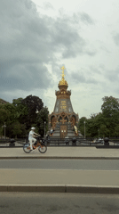 Cyclist rides past golden-cross monument under cloudy skies