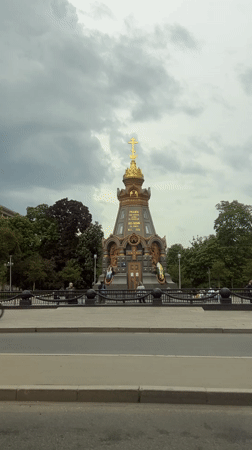 Cyclist rides past golden-cross monument under cloudy skies