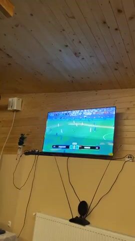 The video shows a wide-angle view of a television screen displaying a soccer match. The score is 0-0, with Paraguay playing against France. The game is in the 30th minute and 23rd second. The players are visible on the green field, wearing white and blue uniforms. The environment appears to be indoors, with wooden walls and ceiling visible above the television. Several black cables are hanging down from the television.
