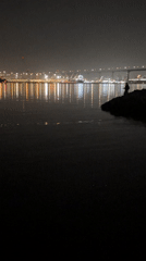 Figure stands on rocks near illuminated bridge in predawn Coronado
