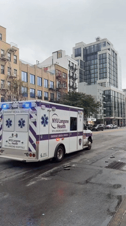 Ambulance lights up a worn, rain-slicked New York street