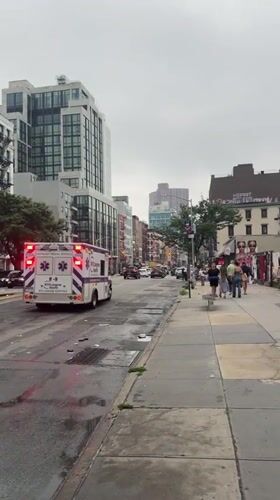 Ambulance lights up a worn, rain-slicked New York street