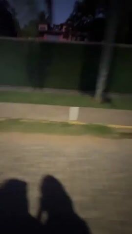 Here's a description of the video:

The video shows a first-person perspective of riding on the back of a scooter at dusk. The scooter has two other riders: the driver, wearing a black helmet, and a child in front of them, also wearing a black helmet. The road is paved with cobblestones and is flanked by trees. Streetlights illuminate the path ahead. The sky is a mix of orange and dark blue, indicating twilight. The camera is shaky, giving the impression of movement.