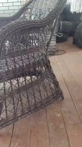 The video pans across a woven chair, showing its intricate pattern and dark brown color. The chair appears to be made of rattan or a similar material. The background is slightly blurred, but suggests an indoor setting with a wooden floor and some objects in the distance, possibly tires. The lighting is dim, creating shadows that highlight the texture of the chair. The camera moves slowly, allowing for a detailed view of the chair's construction.