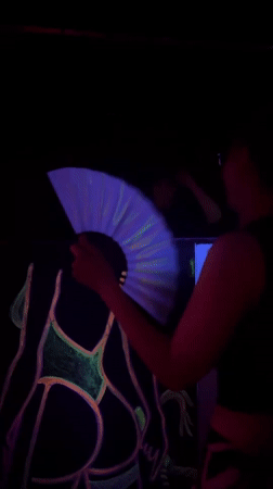 Person waves glowing fan near neon artwork in Varna
