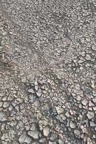 The video shows a close-up, overhead view of dry, cracked earth. The pattern of the cracks creates a mosaic-like texture across the surface. The lighting suggests it is daytime, possibly sunny, as there are subtle shadows cast by the uneven texture of the ground. No people, animals, or specific objects are visible beyond the cracked earth itself. The environment appears to be arid or drought-stricken.