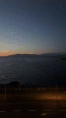 Reykjavik waterfront at twilight, crescent moon over calm water.