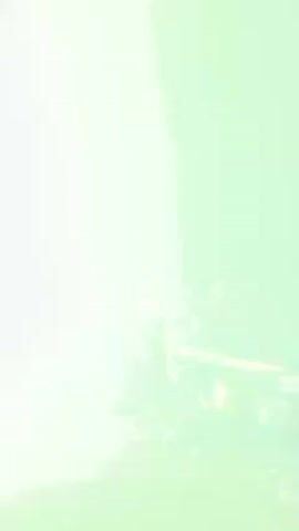 The video appears to capture a live music performance at a concert or club. A DJ, identifiable as a woman, is positioned behind a mixing console. She seems to be actively engaging with the crowd, possibly gesturing or raising her arms. The environment is filled with fog or haze, typical of concert venues, obscuring a full view of the crowd, although their silhouettes and some movement suggest a significant audience. Bright lights, including a blue laser beam, cut through the fog, enhancing the visual atmosphere of the event. The overall scene implies a lively and energetic atmosphere typical of a music performance.