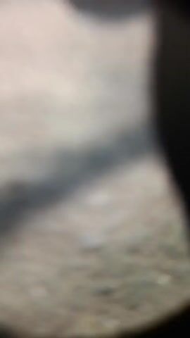 The video begins with a blurry shot of a shadowed area with light filtering through. It then transitions to a slightly clearer view of what appears to be a street or pathway with some debris. The scene then focuses on the lower half of a person wearing white sneakers with fuzzy accents, seated next to a motorcycle. The motorcycle is black and has a license plate that reads "R 5288 HK." The camera then pans up to reveal a woman wearing a traditional headdress with feathers and a dark hijab, along with a costume that includes a fur-like collar. She is seated, and a motorcycle with the license plate "R 4193 BK" is visible in the foreground. Behind her, there are banners with text, some of which appear to be advertisements. The overall environment seems to be an outdoor setting, possibly a market or event.