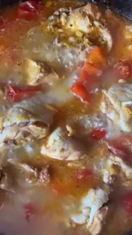 A close-up shot shows a simmering dish containing chunks of chicken and diced red tomatoes in a light-brown broth. The food is bubbling gently in a dark pan.